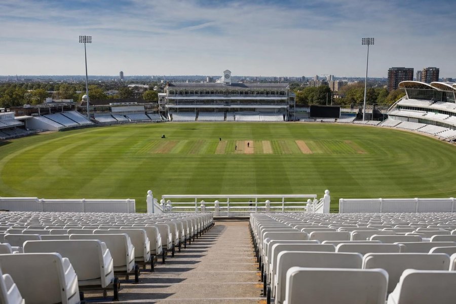 An empty cricket ground before a match with the covers off, the pitch lit by a low sun, a sightscreen and rows of empty seats. (AI-generated image)