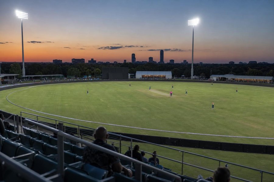 A new floodlit cricket ground in Texas at dusk, a temporary stadium with bleachers, warm sky and an American suburban skyline. (AI-generated image)